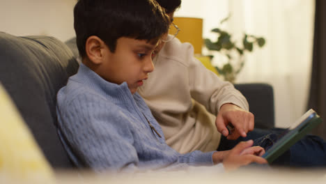 Two-Young-Boys-Sitting-On-Sofa-At-Home-Playing-Games-Or-Streaming-Onto-Digital-Tablet-2